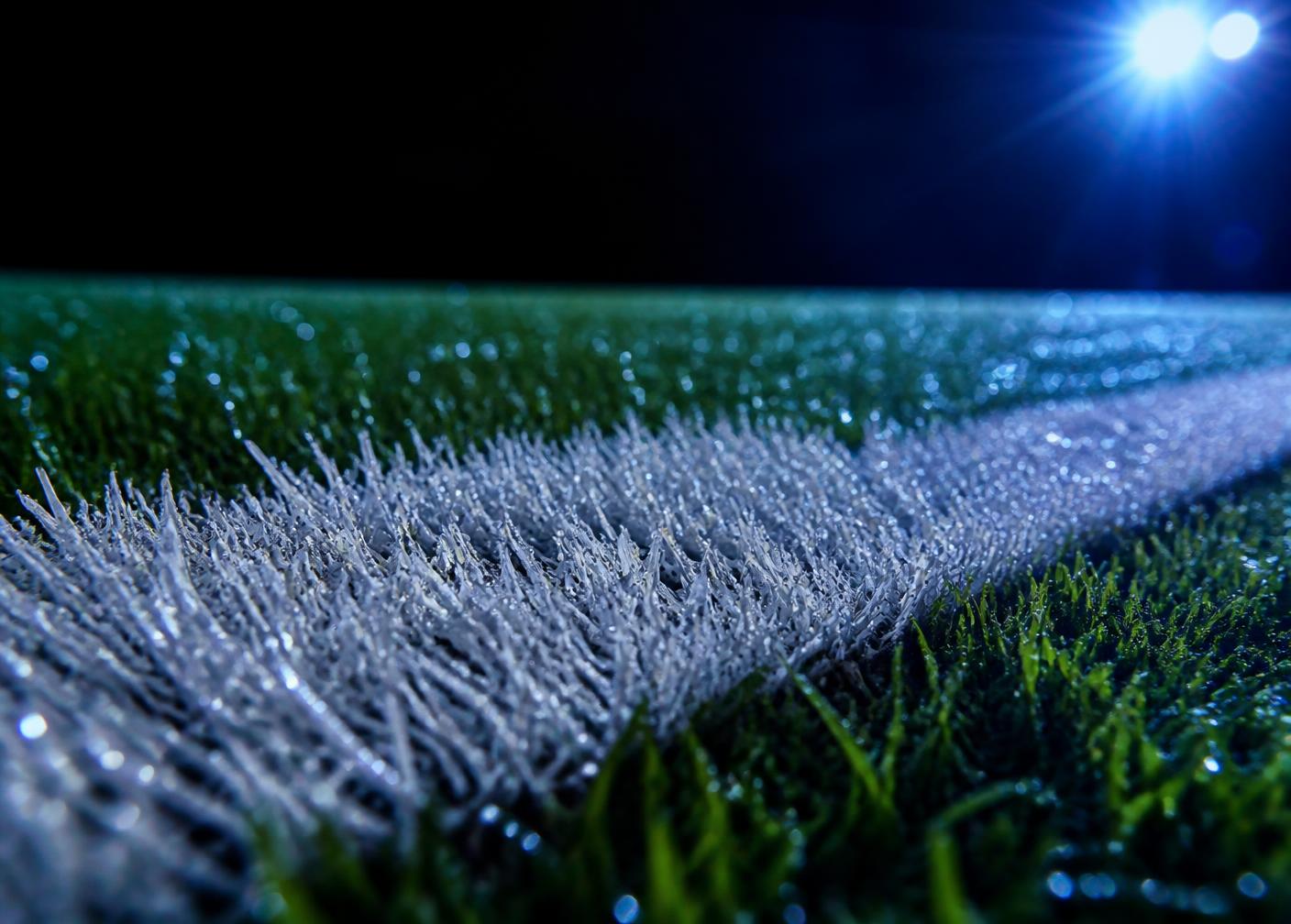 Close up of a floodlit pitch marking on wet grass at night